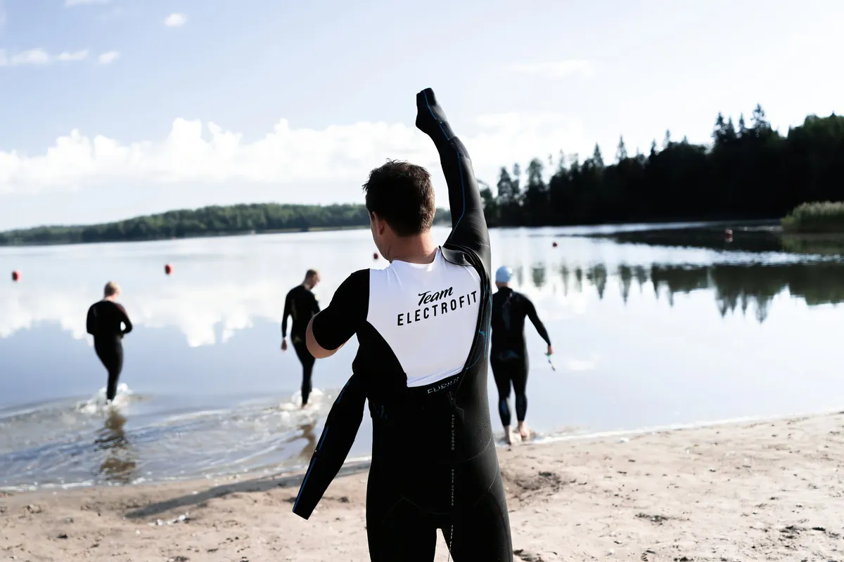 Triathlonisteja märkäpuvuissa järven rannalla ennen uintia