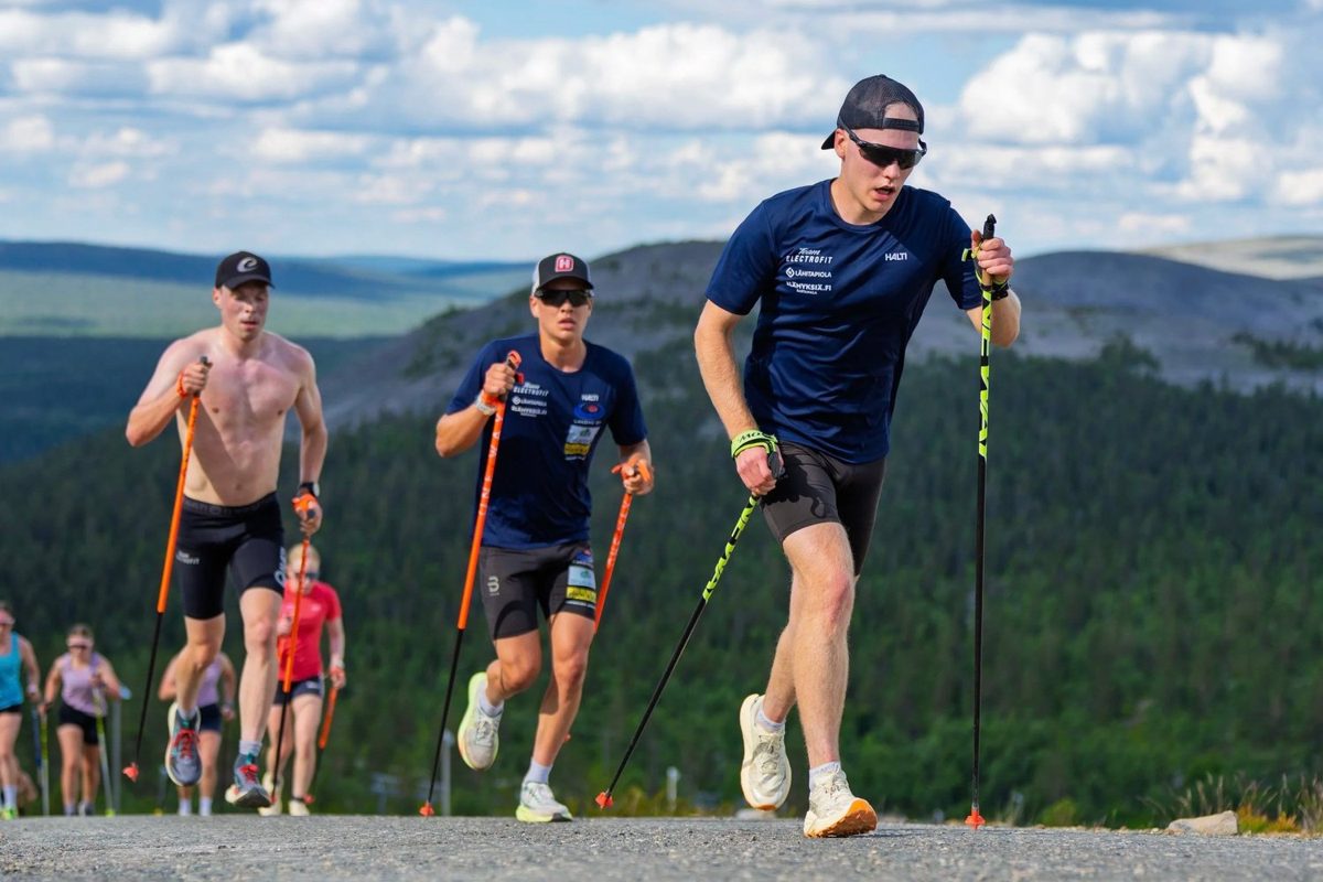 Juoksijoita sauvojen kanssa ylämäessä tunturimaisemassa.